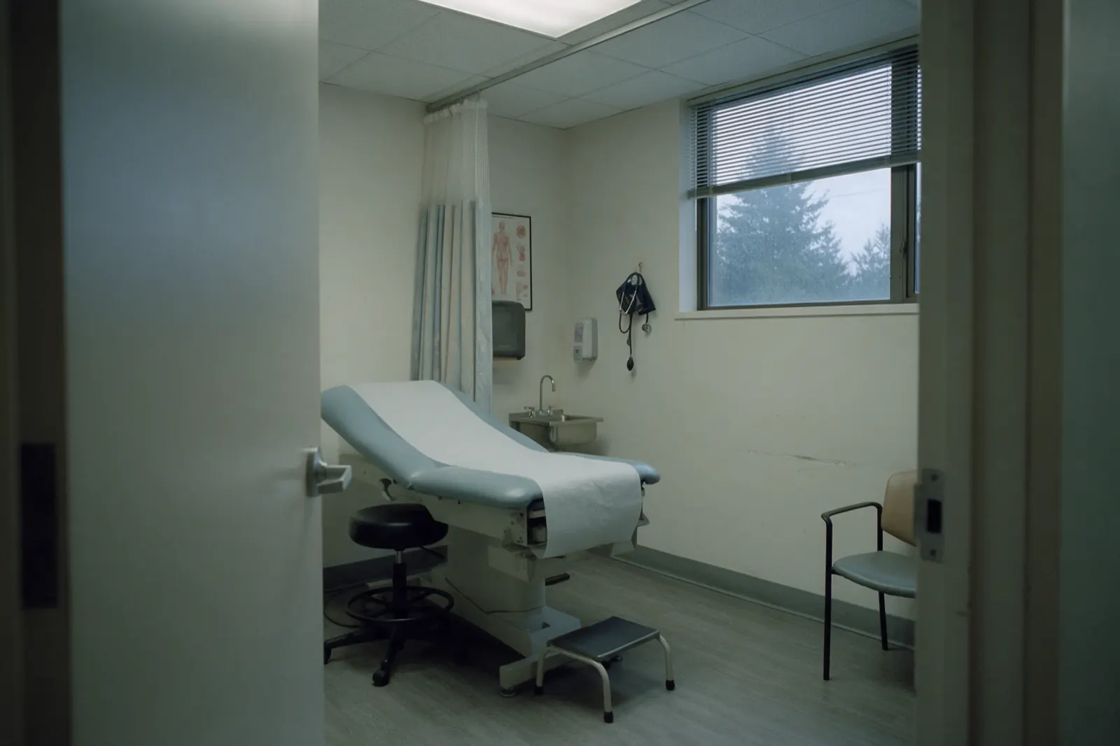 An empty clinic examination room set up between appointments, with a fresh paper roll on the examination table.
