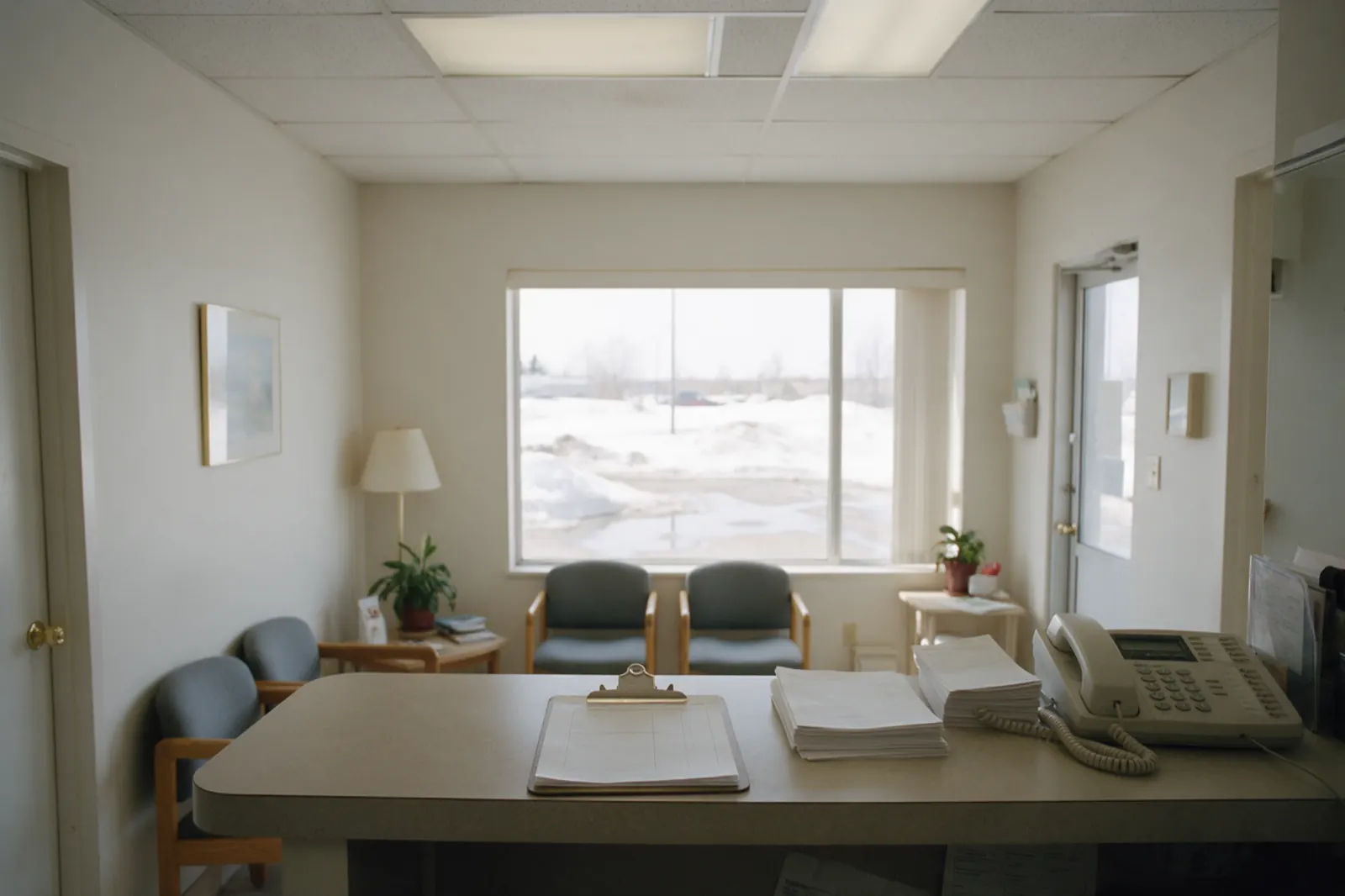 The reception desk stands empty between appointments, a sign-in clipboard squared on the counter and a stack of blank forms beside it.