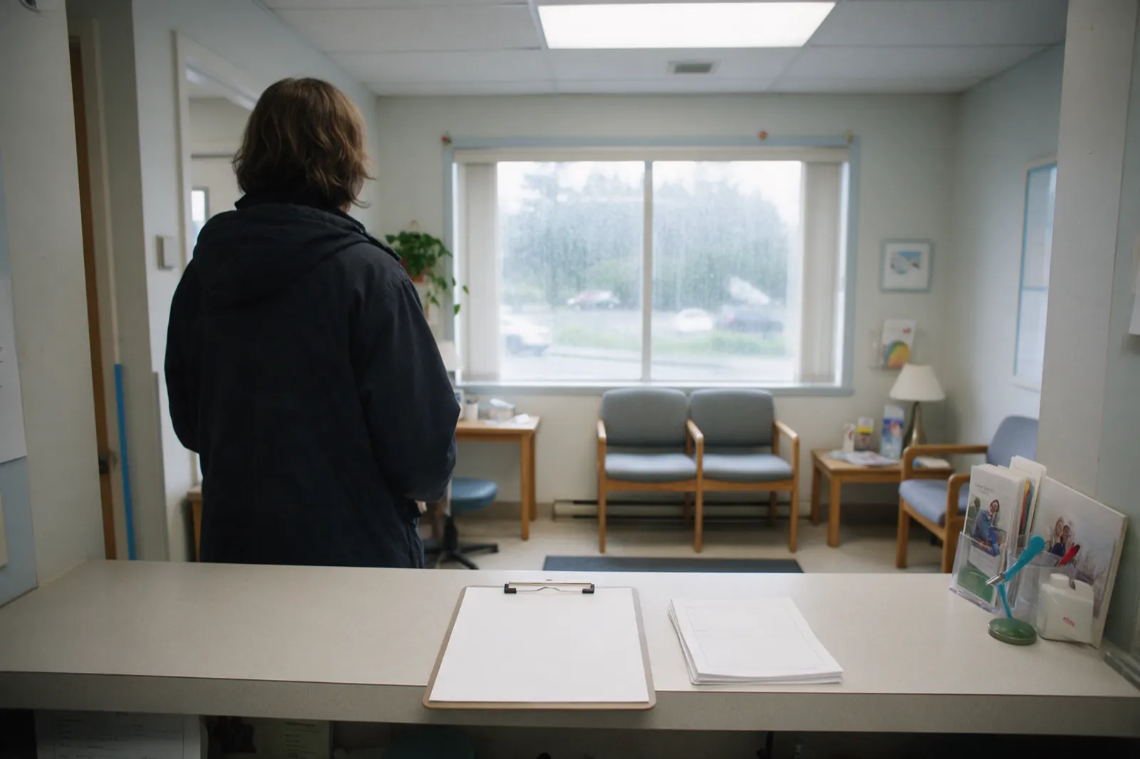 The reception desk stands empty between appointments, a sign-in clipboard squared on the counter and a stack of blank forms beside it.