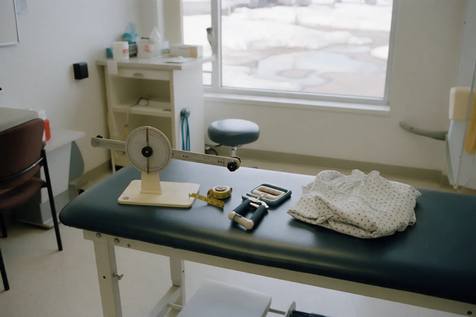 A goniometer, a tape measure and a hand dynamometer lie on a clean bench beside a folded gown.
