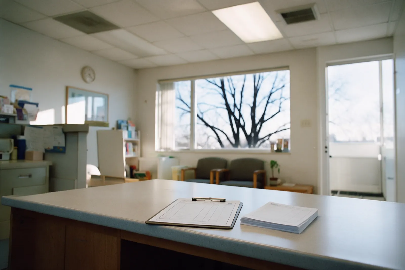The reception desk stands empty between appointments, a sign-in clipboard squared on the counter and a stack of blank forms beside it.