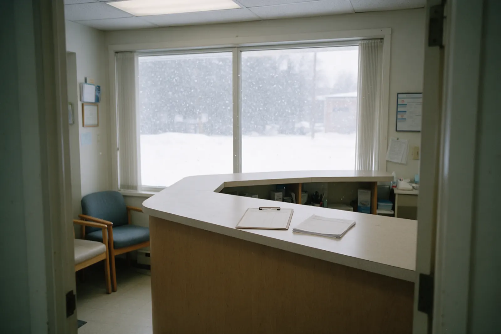 The reception desk stands empty between appointments, a sign-in clipboard squared on the counter and a stack of blank forms beside it.